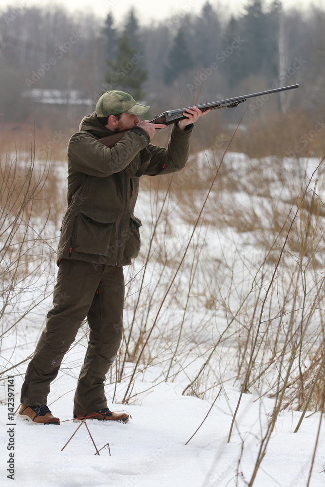 Fototapeta premium Hunter man with shotgun dressed in dark khaki clothing in the forest