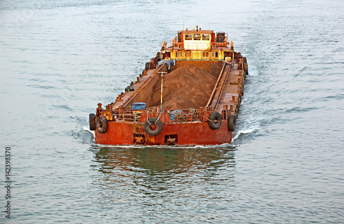 Large cargo barge transporting iron ore mined in hinterland to the main harbor for loading into big ships for exporting, along Mandovi River in Goa, India