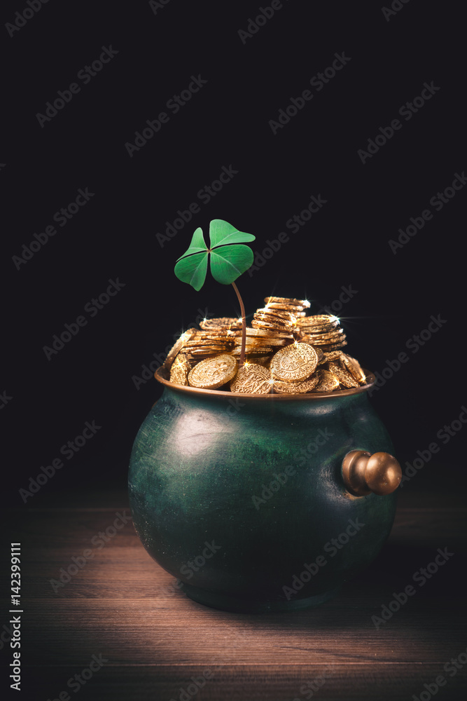 pot full of gold coins with a four leaf clover on a wooden surface and ...