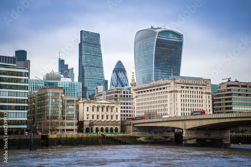 London, England - Iconic red double-decker buses on London Bridge with office buildings and famous skyscrapers at background