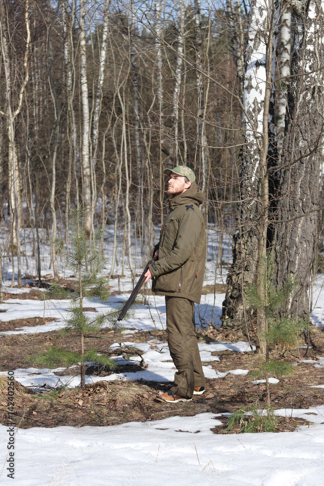 Hunter man with shotgun dressed in dark khaki clothing in the forest