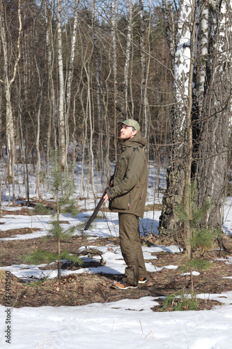 Hunter man with shotgun dressed in dark khaki clothing in the forest