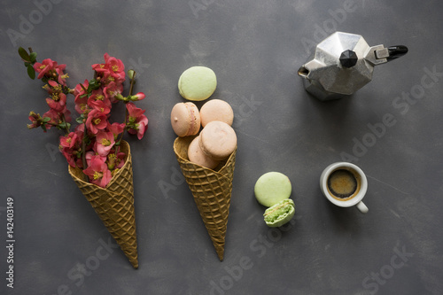 Coffee, macarons and flowers in ice cream cone on cement background