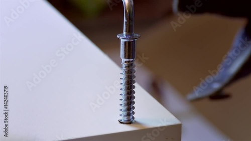 Wood Furniture / Screw Driver / DIY Home. Worker in gloves tightening the metal screw in the chipboard panel, while constructing white shelving.