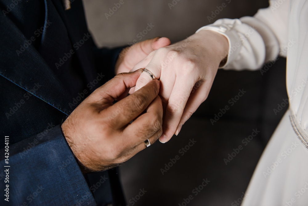 The groom wears an engagement ring on the finger of the bride