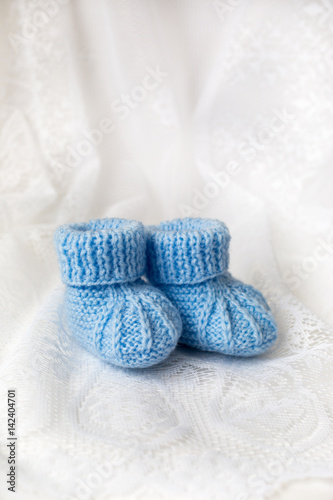 Knitted blue baby booties on lace background