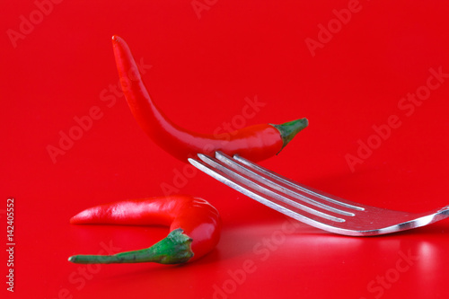Red hot chili pepper on vintage silver fork over red background