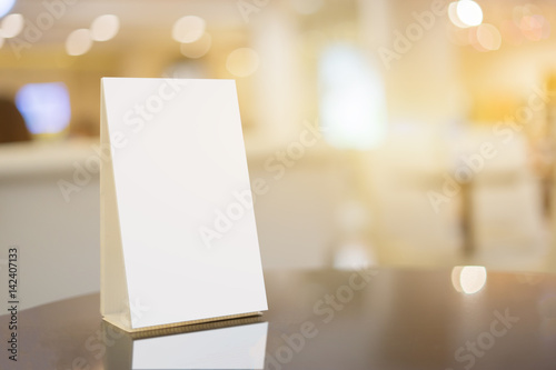 Mock up Menu frame on Table in Bar restaurant ,Stand for booklets with white sheets of paper acrylic tent card on cafeteria blurred ,Chef cooking in background. © Have a nice day 