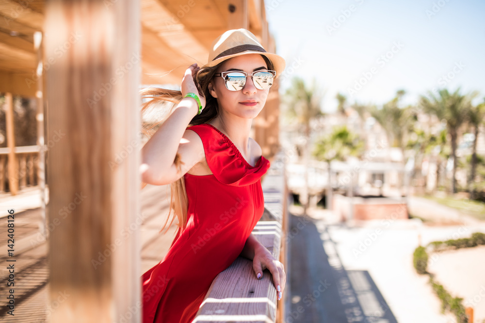 Young white girl standing on the pier in a red sun dress and hat.
