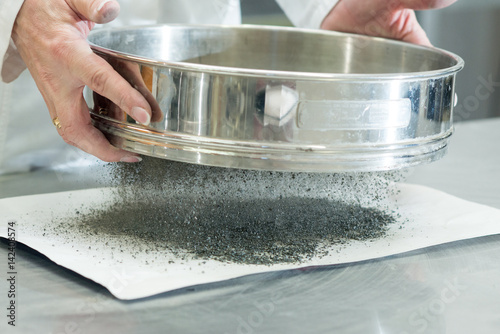 On site road testing laboratory. Placing sample of gravel into a silver container. Preparation step - pouring sample of a layer of soil