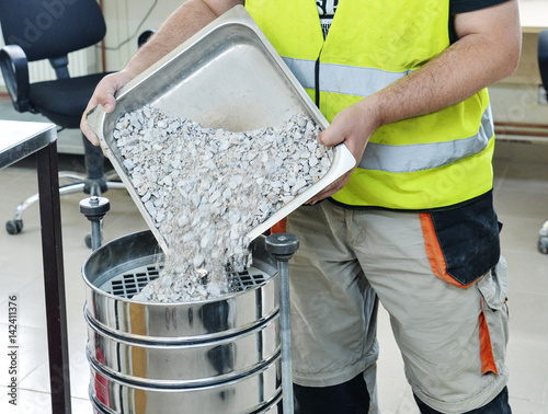 On site road testing laboratory. Placing sample of gravel into a silver container. Preparation step - pouring sample of a layer of soil