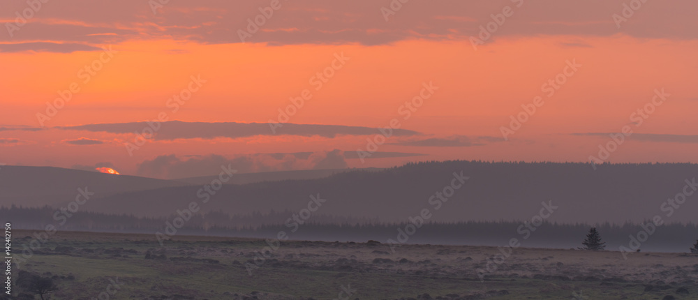 Sunset over Dartmoor National Park. Last moments of setting sun over Dartmoor Forest on misty evening in National Park in Devon, England, UK