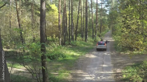 Flying over the car in forest. The quadcopter follows the jeep on the nature in forest. Aerial survey of jeep off-road. Car goes through the forest view photo