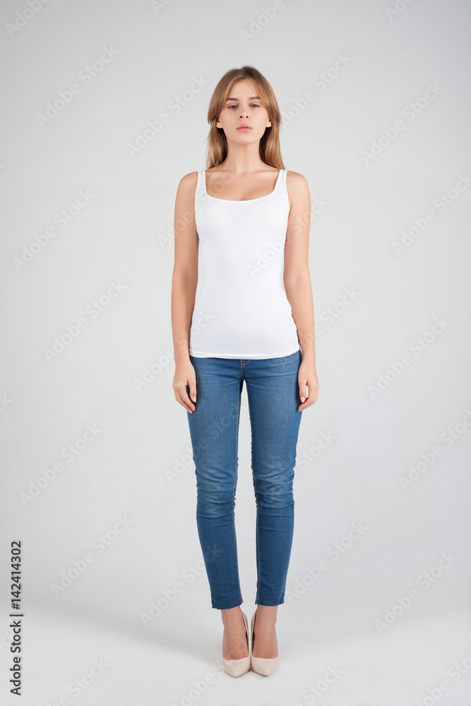 Beauty studio portrait of blond girl with long straight hair with natural makeup in white shirt blue jeans at silver background. Vogue style portait. Space in background for copy, text, your words. Beauty studio portrait of blond girl with long straight hair with natural makeup in white shirt blue jeans at silver background. Vogue style portait. Space in background for copy, text, your words.