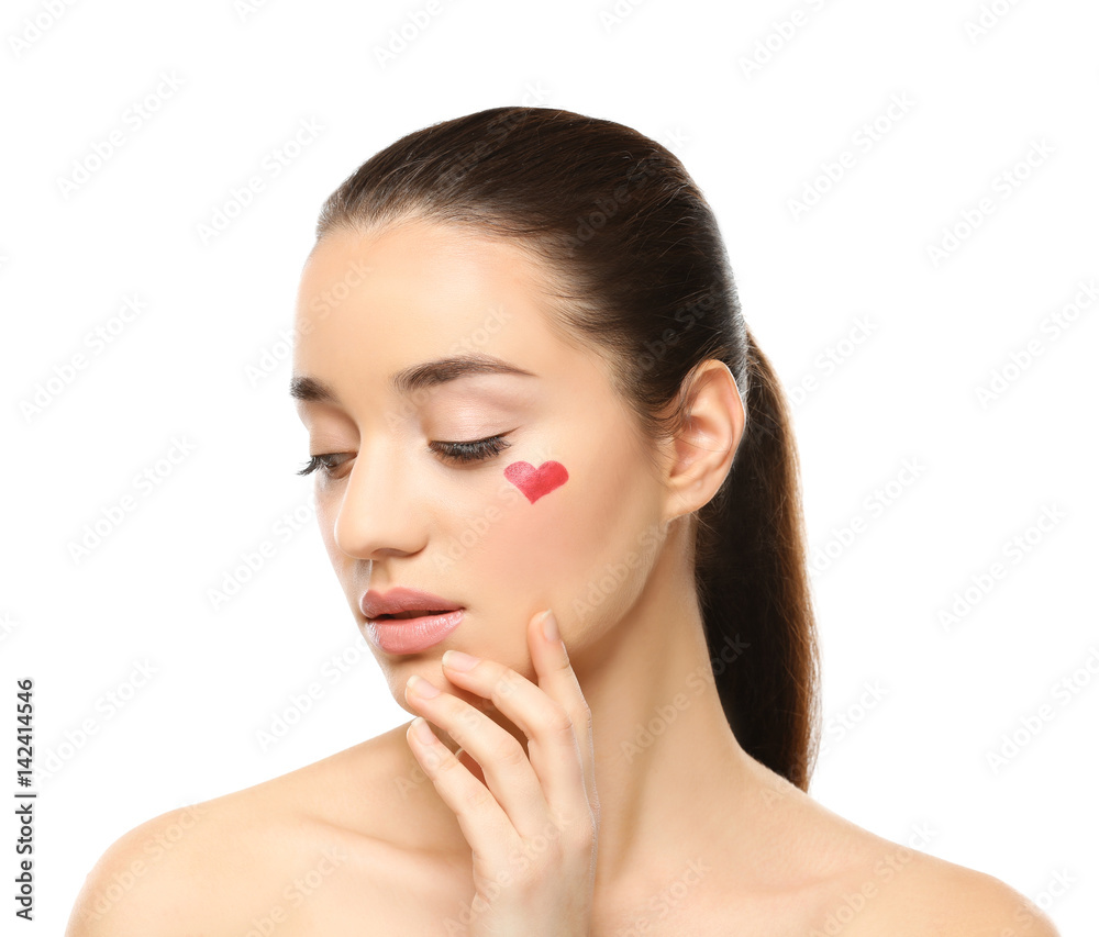 Beautiful young woman with heart painted on face, against white background