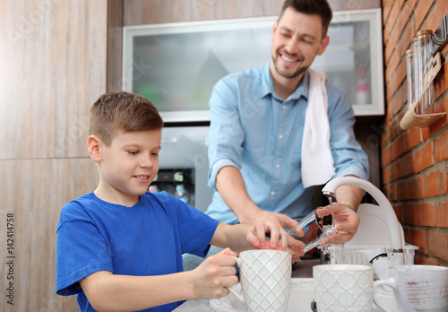 Fotografie Dad and son doing the washing up in kitchen