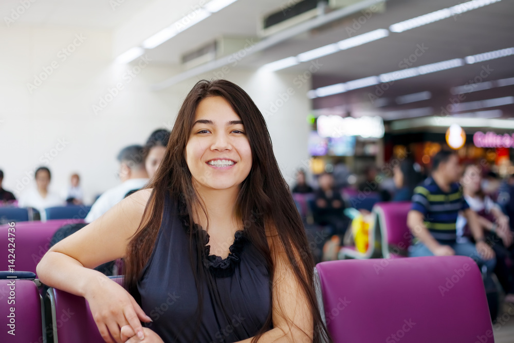 Teen girl sitting at airport departure lounge, smiling
