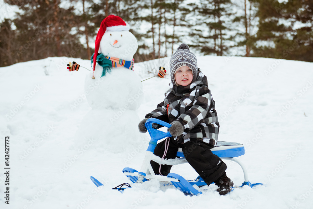 Cute little boy in winter clothes outdoors. Child on a sled or snowmobile.