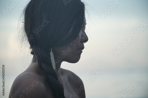 Asiatische Frau mit Zopf und Feder als Ohrring im silber-blauen Licht von Thailand