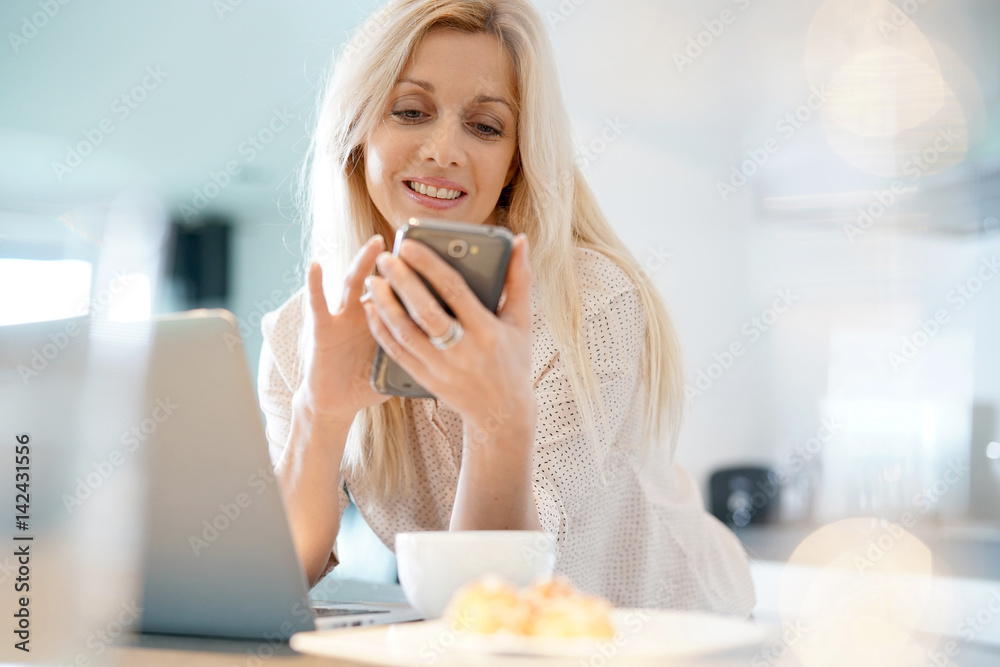 Blond woman with eyeglasses connected on smartphone at home Blond woman with eyeglasses connected on smartphone at home