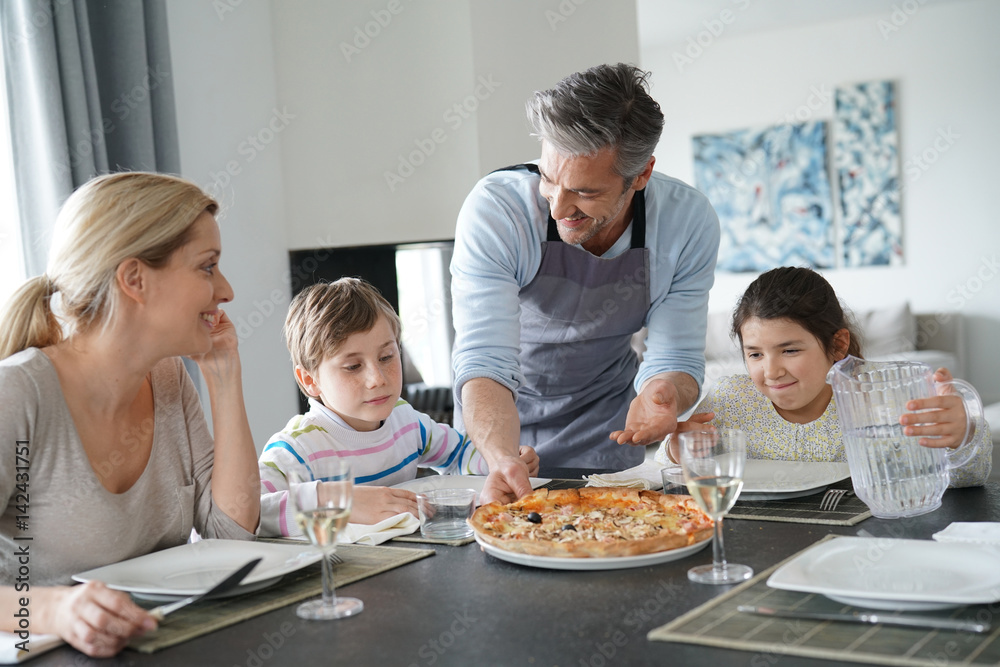 Dad serving pizza to family at dining table