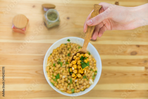 Spoonful of chick peas. Top view of cheak peas in wood spoon held in hand above the table and bowl of raw chicklings photo