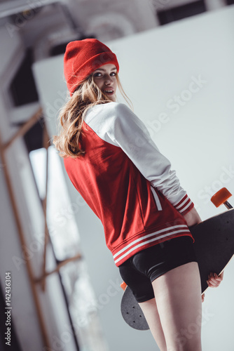 Stylish hipster woman with longboard posing in studio on grey photo