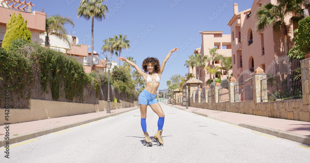 Female wearing shorts and blue knee-high socks riding on roller skates with hands up on city background. 