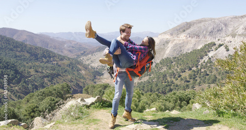 Young loving man holding girlfriend on hands and both laughing with mountainscape on background. © Dash