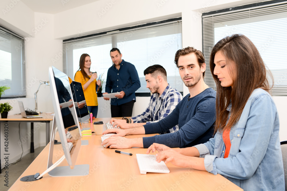 portrait of a handsome young man in high school classroom working in computer on row with teacher and classmates in background portrait of a handsome young man in high school classroom working in computer on row with teacher and classmates in background