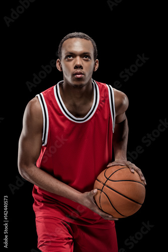 Young sportsman in uniform playing basketball with ball on black