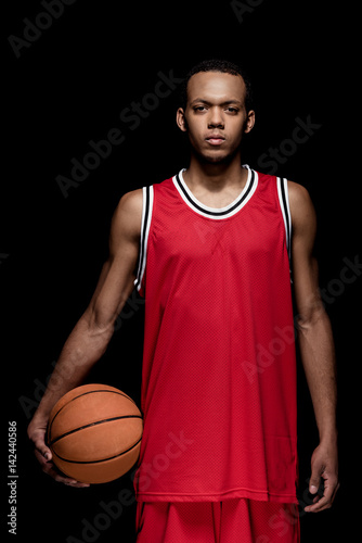Young athletic man basketball player standing with ball on black