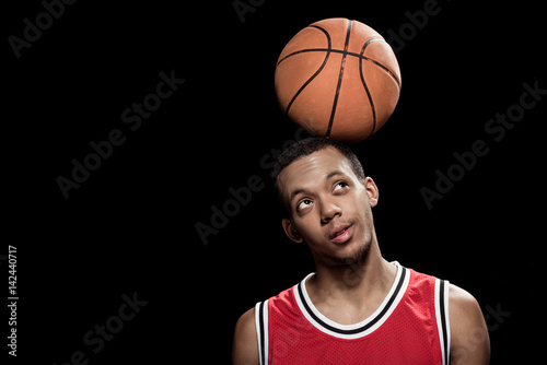 African american basketball player posing and balancing ball on head on black