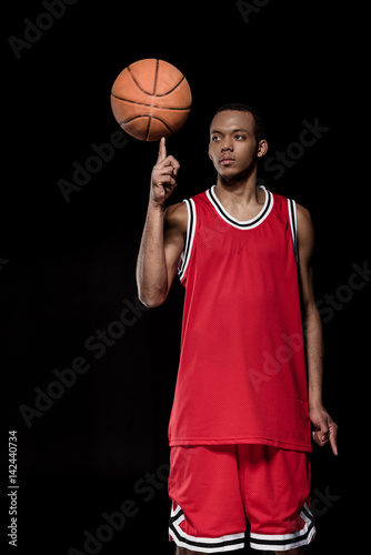 African american basketball player posing and balancing ball on finger on black