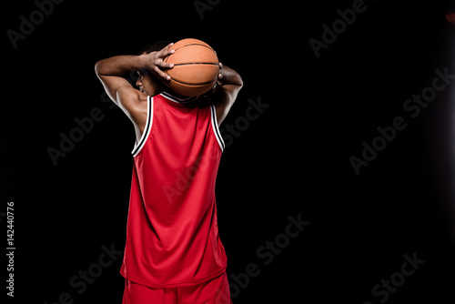 Back view of african american basketball player throwing ball on black