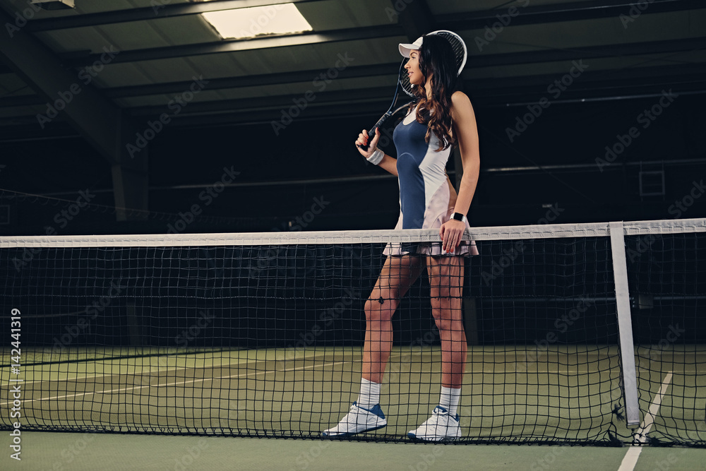 Female tennis player posing on an indoor tennis court.