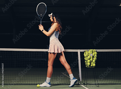 Female tennis player posing on an indoor tennis court.