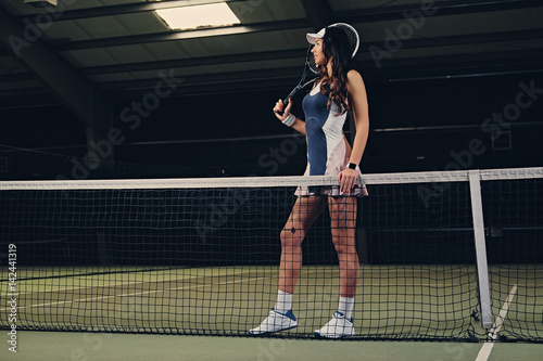 Female tennis player posing on an indoor tennis court.