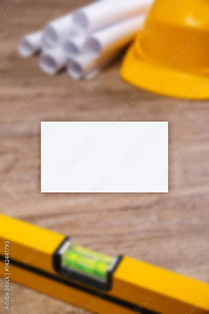 Business card mockup. Helmet, paper plans and building level. Construction design. Wood rustic background.