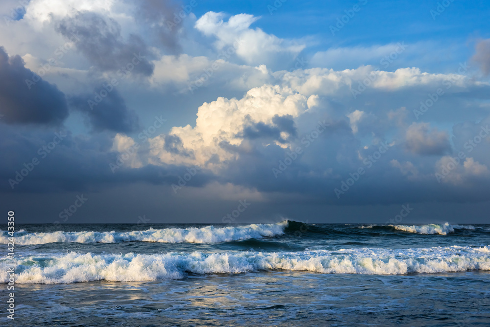 Dramatic nature background. Breaking ocean waves under colorful cloudy sky in the sunny morning