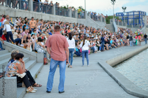 A large gathering of people. Back men on the background of people. People on the promenade waiting for the concert