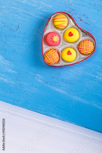 Macaroon cakes. Colorful almond macaron cookies. Love heart-shaped delivery box. Different flavors. On blue wooden rustic background.