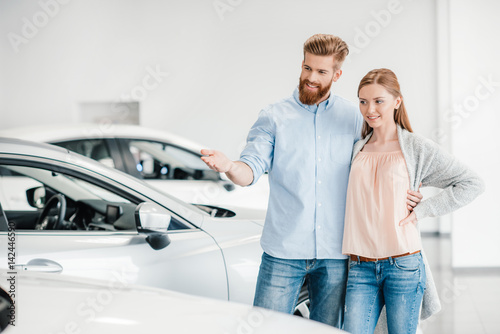Happy couple choosing car in dealership salon, man pointing on car