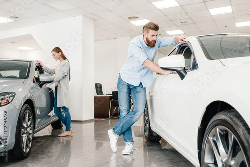 Φωτογραφία Couple choosing car, man and woman looking on various cars in dealership salon