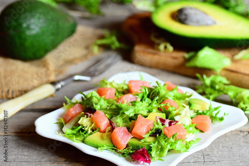 Salmon, avocado and mixed lettuce salad. Quick salad with salmon slices, fresh avocado and lettuce leaves mix on a plate. Avocado and half, fork on a vintage wooden table. Closeup