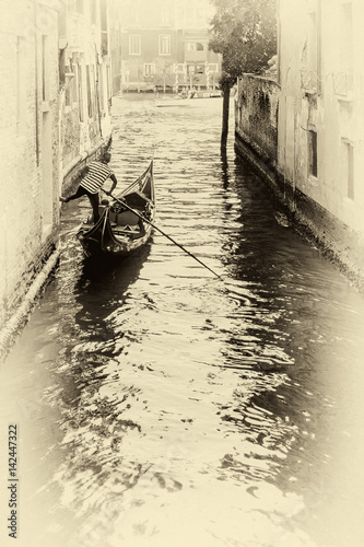 Artistic view of a gondolier leaning one leg on a wall of the Rio San Falice to give himself a boost towards the Grand Canal of Venice, Italy photo