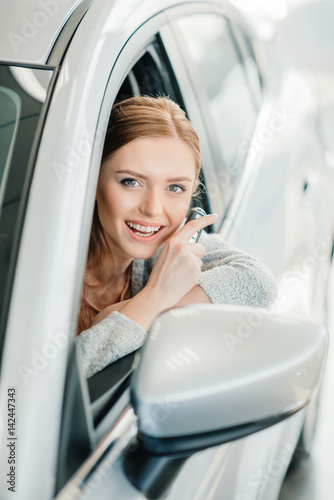 Attractive smiling young woman sitting in new car and holding key