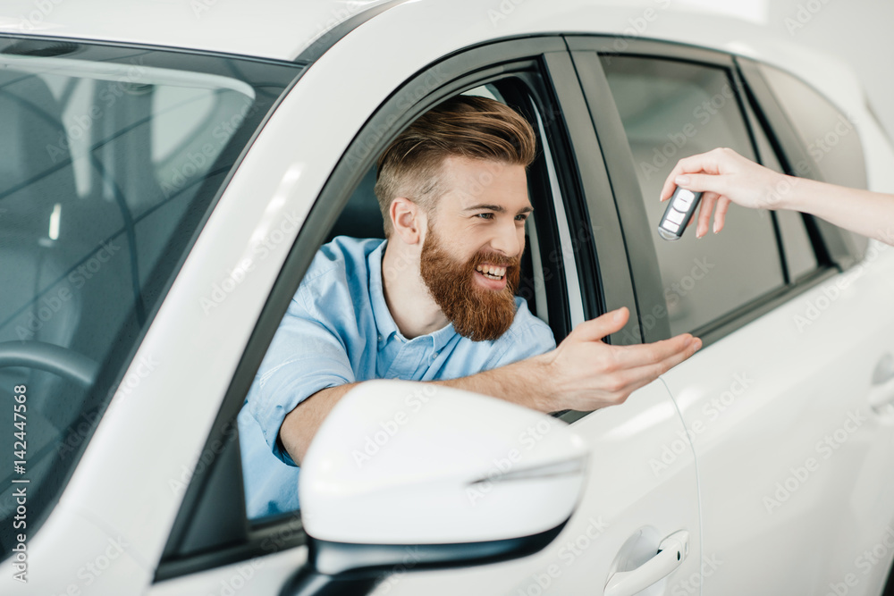 Seller giving key to happy young bearded man sitting in new car Seller giving key to happy young bearded man sitting in new car