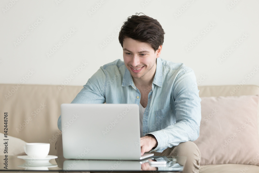 Young handsome man smiling looking at screen of laptop computer, chatting online, working, texting, commenting social networks. Long distance relationship, technology and lifestyle Young handsome man smiling looking at screen of laptop computer, chatting online, working, texting, commenting social networks. Long distance relationship, technology and lifestyle