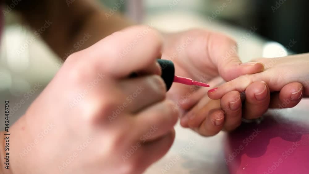 Nail artist doing manicure for little girl in professional salon. Close up view of manicure master applying gel polish. Hands close up view Nail artist doing manicure for little girl in professional salon. Close up view of manicure master applying gel polish. Hands close up view